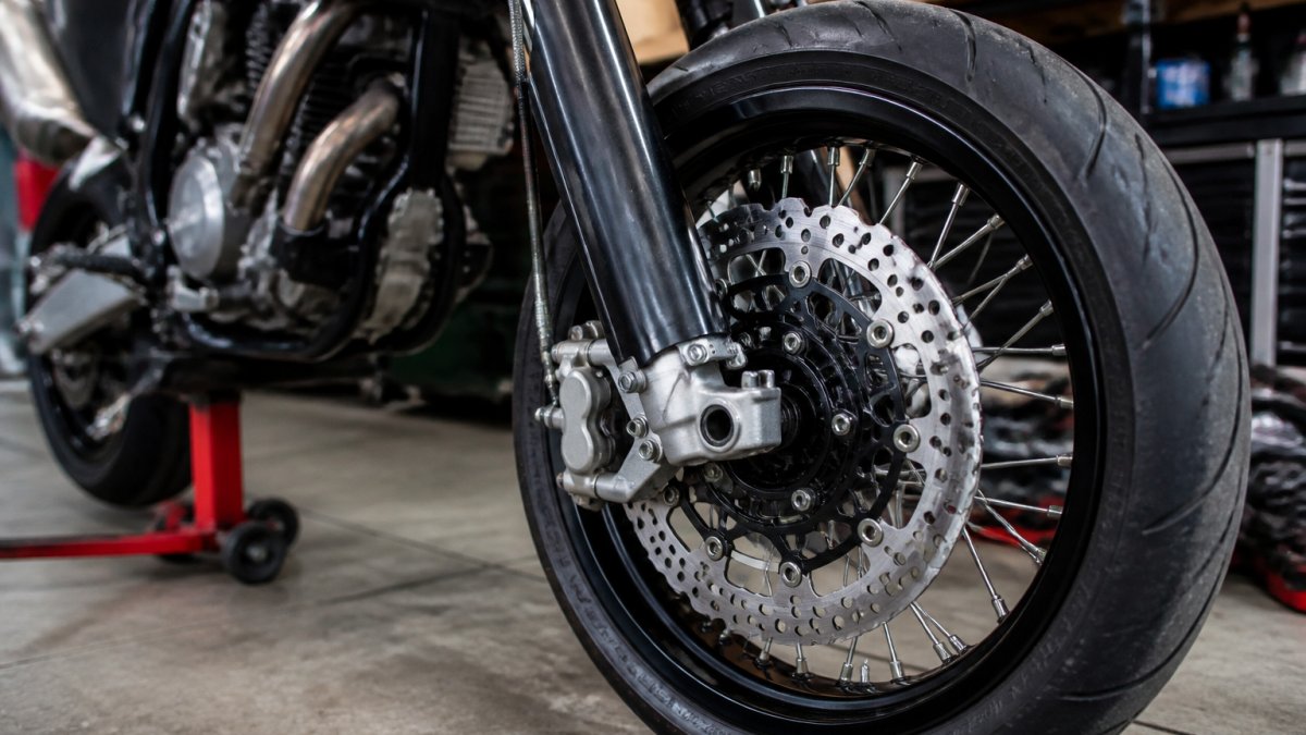 Close-up of a supermoto wheel featuring big brake kits with a drilled rotor and radial caliper in a workshop.